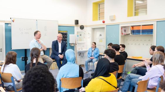 Schülersprechstunde in der Realschule Stadtmitte mit Oberbürgermeister Marc Buchholz und Lehrer Thomas Kretzschmar (sitzen vorn), die mit einer Gruppe von Schüler*innen im Stuhlkreis sprechen.