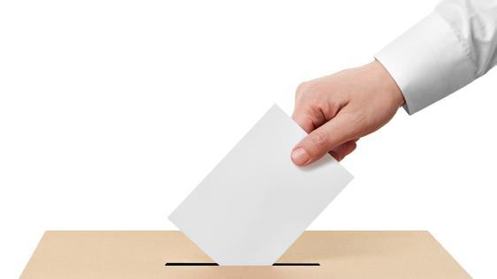 eine Person wirft einen Wahlbrief in eine Urne
