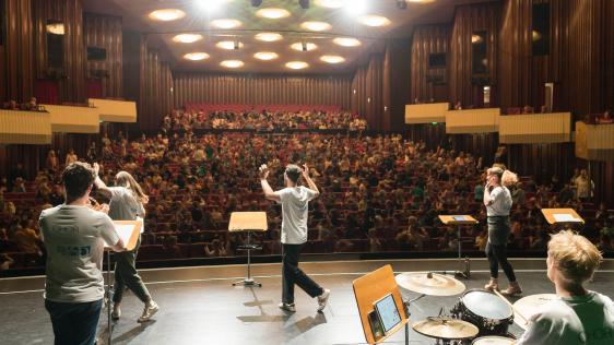 Singleiter*innen unterstützen die Grundschulkinder beim Vortragen der eingeübten Lieder während des Sing-Pausen Konzerts am 11.06.2024 in der Stadthalle.