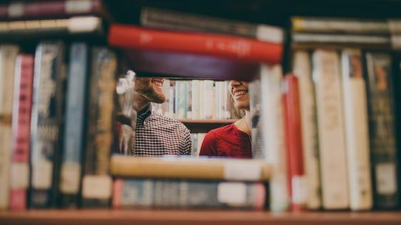 Sicht durch ein Bücherregal: Schülerin und Schüler in der Bibliothek.
