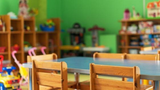 Blick auf einen Kindertisch mit Holzstühlen in einem eingerichteten Kindertagespflege-Raum. Kita, Kinderbetreuung, Prüfung der Eignung von Bewerberinnen und Bewerbern für die Tätigkeit als Tagesmutter oder Tagesvater