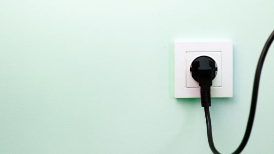Im Hintergrund eine grüne Wand, davor ist eine weiße Steckdose mit einem schwarzen Stecker zu sehen