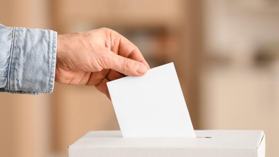 eine Person wirft einen Wahlbrief in eine Urne
