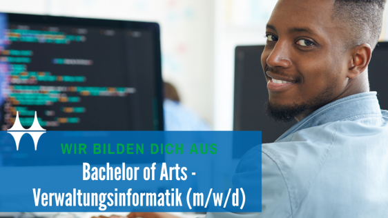 Das Bild zeigt einen jungen Mann sitzend an einem Tisch. Er dreht sich in die Kamera und lächelt. Auf dem Tisch steht ein Monitor und eine Tastatur. Der Monitor zeigt einen bunten Programmtext.