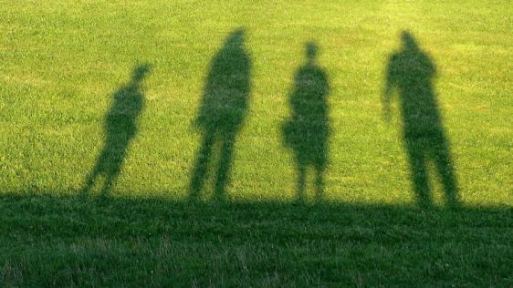 Grüne Wiese, auf die der Schatten von 4 unterschiedlich großen und alten Personen. Familien, Hilfen, Erziehung, Psychologisches Beratungszentrum, Erziehungsberatungsstelle.