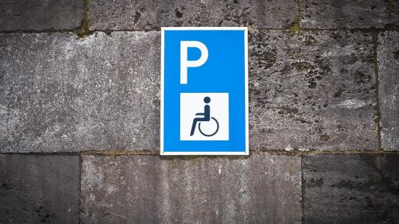 Schild eines Behindertenparkplatzes mit Rollstuhlfahrersymbol an einer Steinwand.