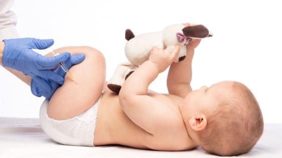 Ein Baby wird beim Arzt geimpft. Es hält dabei ein Stofftier in der Hand. 