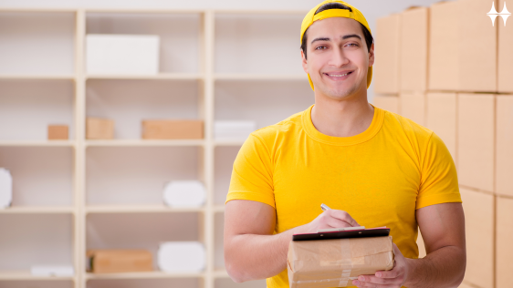 Das Bild zeigt einen jungen Mann der vor einem Regal mit Paketen steht. Er lächelt in die Kamera und hält ein Paket in den Händen.