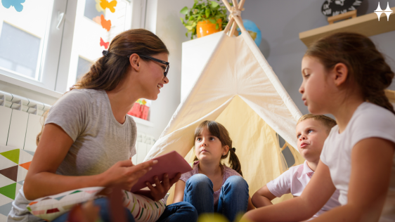 Das Bild zeigt eine junge Frau, die einer Gruppe von drei Kindern eine Geschichte vorliest. Alle sitzen im Kreis vor einem Tipi.