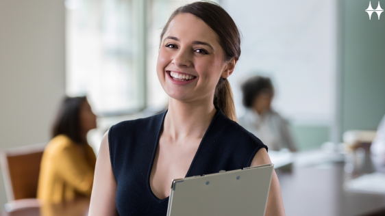 Das Bild zeigt eine junge Frau, die in die Kamera lächelt. Sie hält ein Klemmbrett in den Händen