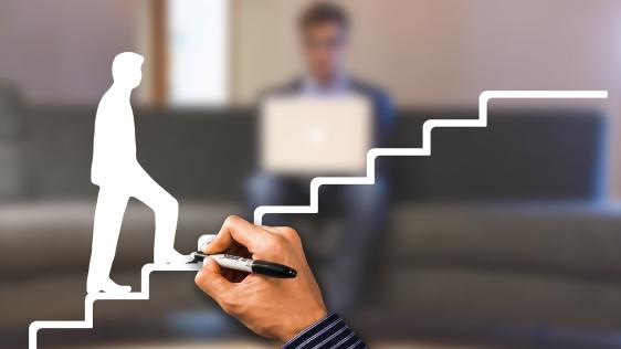 Das Bild zeigt eine Hand, die eine Treppe malt. Eine männliche Person geht diese Treppe nach oben. Im Hintergrund sitzt ein Mensche mit einem Laptop auf der Couch