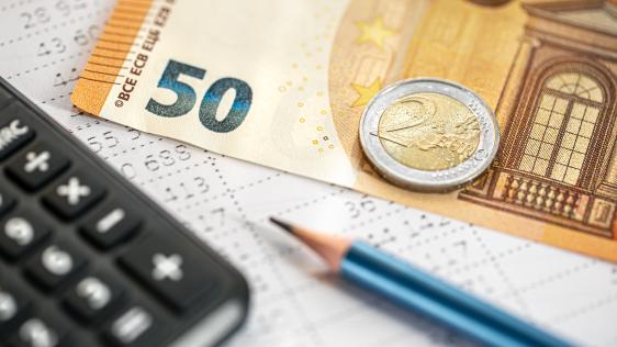 Auf einer unscharfen Gehaltsabrechnung liegen ein Taschenrechner, Geld und ein Bleistift