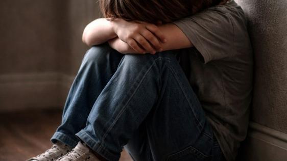 Verzweifeltes Kind, das auf dem Boden sitzt und das Gesicht in seine Hände gräbt.