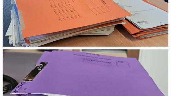 Akten mit orangenem und violetten Einband auf Schreibtischen