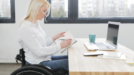 Seitenansicht einer Frau im Rollstuhl die an einem Schreibtisch arbeitet