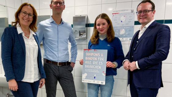 Die Personen stellen den Spender mit den Periodenprodukten am Gymnasium Heißen vor.