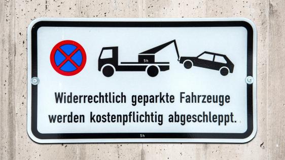Schild an einer Mauer mit dem Hinweis, dass widerrechtlich abgestellte Fahrzeuge kostenpflichtig abgeschleppt werden.