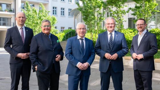 Verwaltungsvorstand steht vor grünem Hintergrund im Innenhof des Rathauses