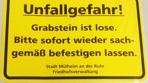 Ein gelber Hinweis-Aufkleber, der darauf hinweist, dass ein Grabstein lose ist.