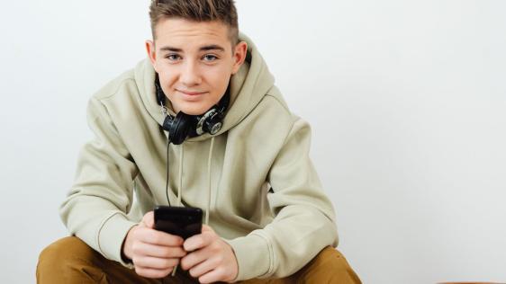 Ein Teenager sitz mit Handy auf einer Couch.