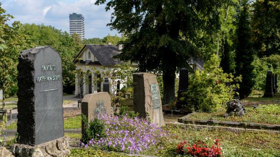 Historische Grabstätten auf dem Altstadtfriedhof vor der Trauerhalle. Im Hintergrund einer der Türme am Hans-Böckler-Platz