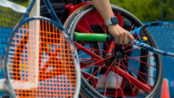 Ein Rollstuhlfahrer ist auf dem Tennisplatz und hält einen Schläger in der Hand.