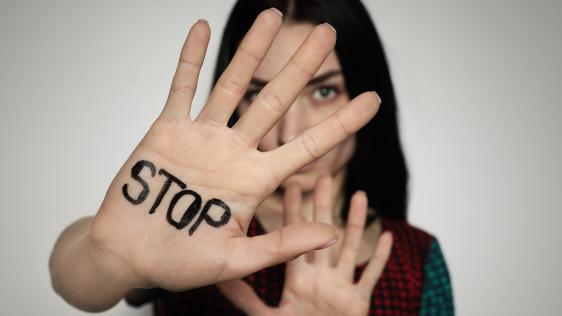 Eine Frau hält ihre Hand abwehrend vor ihr Gesicht. Auf der Hand steht STOP.