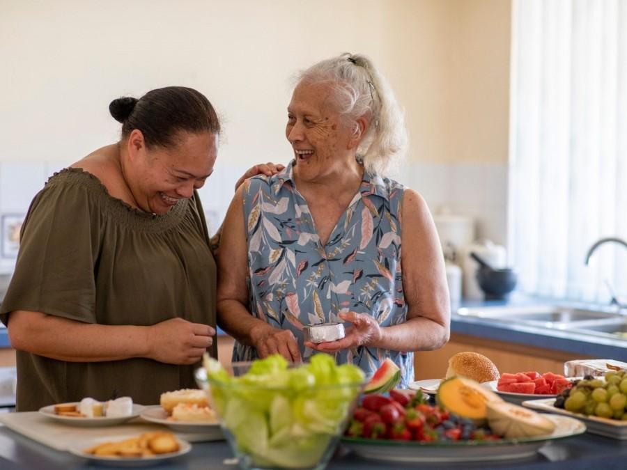 Betreuerin und ältere Dame kochen und lachen zusammen. Informationen zu Entlastung im Alltag bei der Haushaltsführung, Entlastung im Alltag durch individuelle Hilfen. Senioren, Seniorinnen