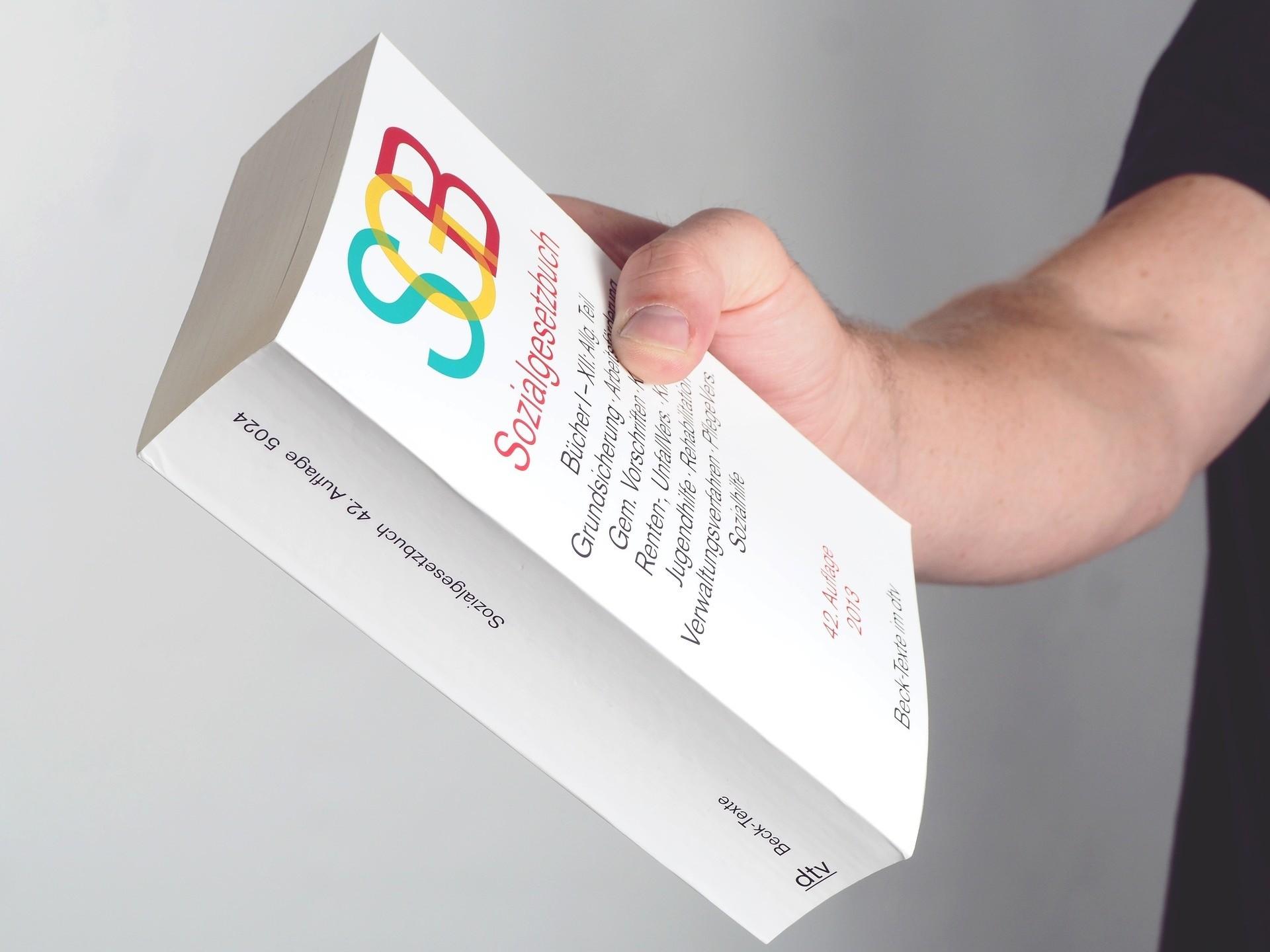 Person hält das Sozialgesetzbuch - SGB - in der Hand. Leistungsgewährung, Hilfebedürftige, Soziales, Sozialagentur