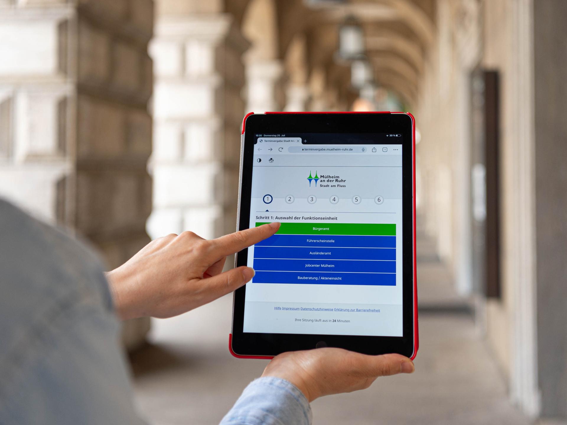 Auf dem Tablet wird das Serviceportal aufgerufen, im Hintergrund ist das Rathaus zu sehen.