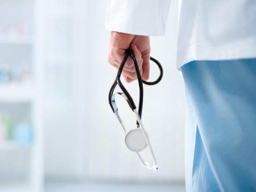 Die Rückseite eines Arztes im Flur eines Krankenhauses. Er hält ein Stethoskop in der Hand.