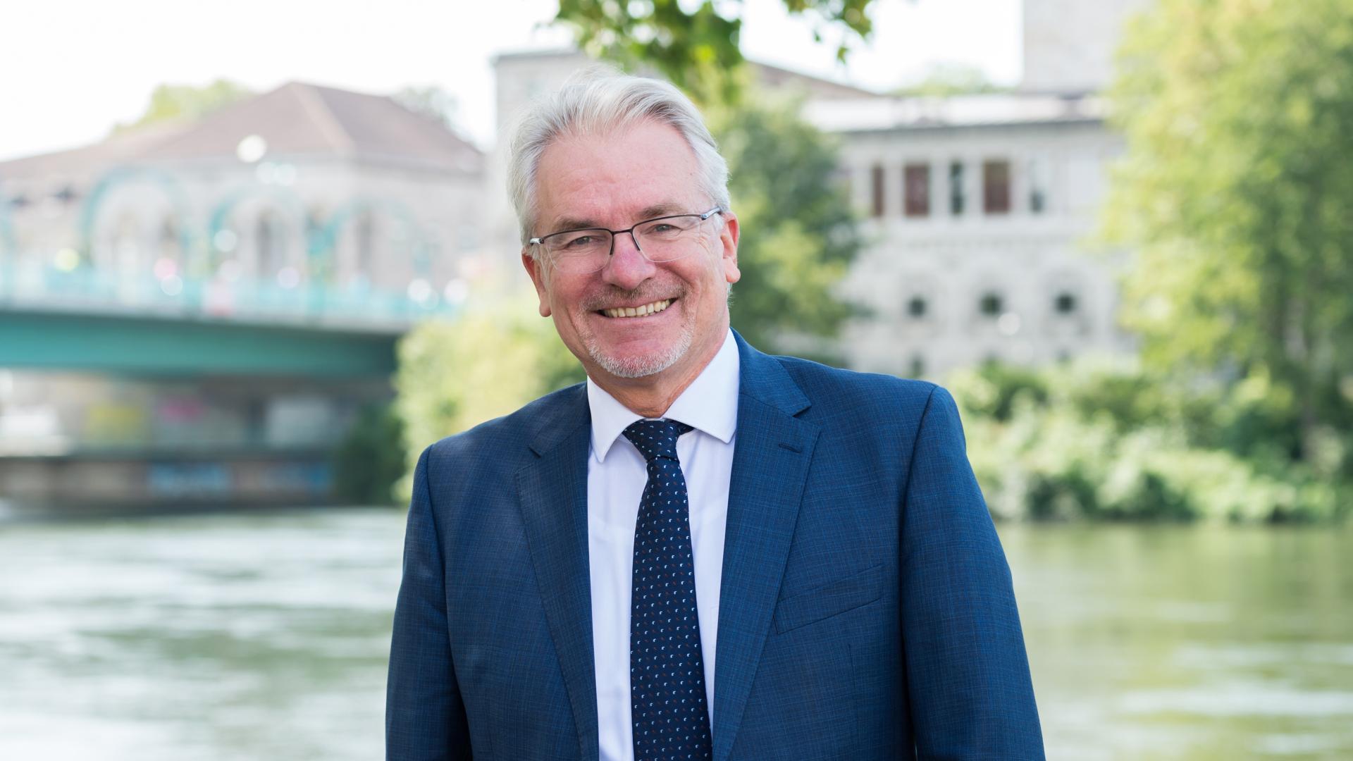 Oberbürgermeister Marc Buchholz steht im Grünen an der Ruhr, im Hintergrund ist die Stadthalle zu sehen.