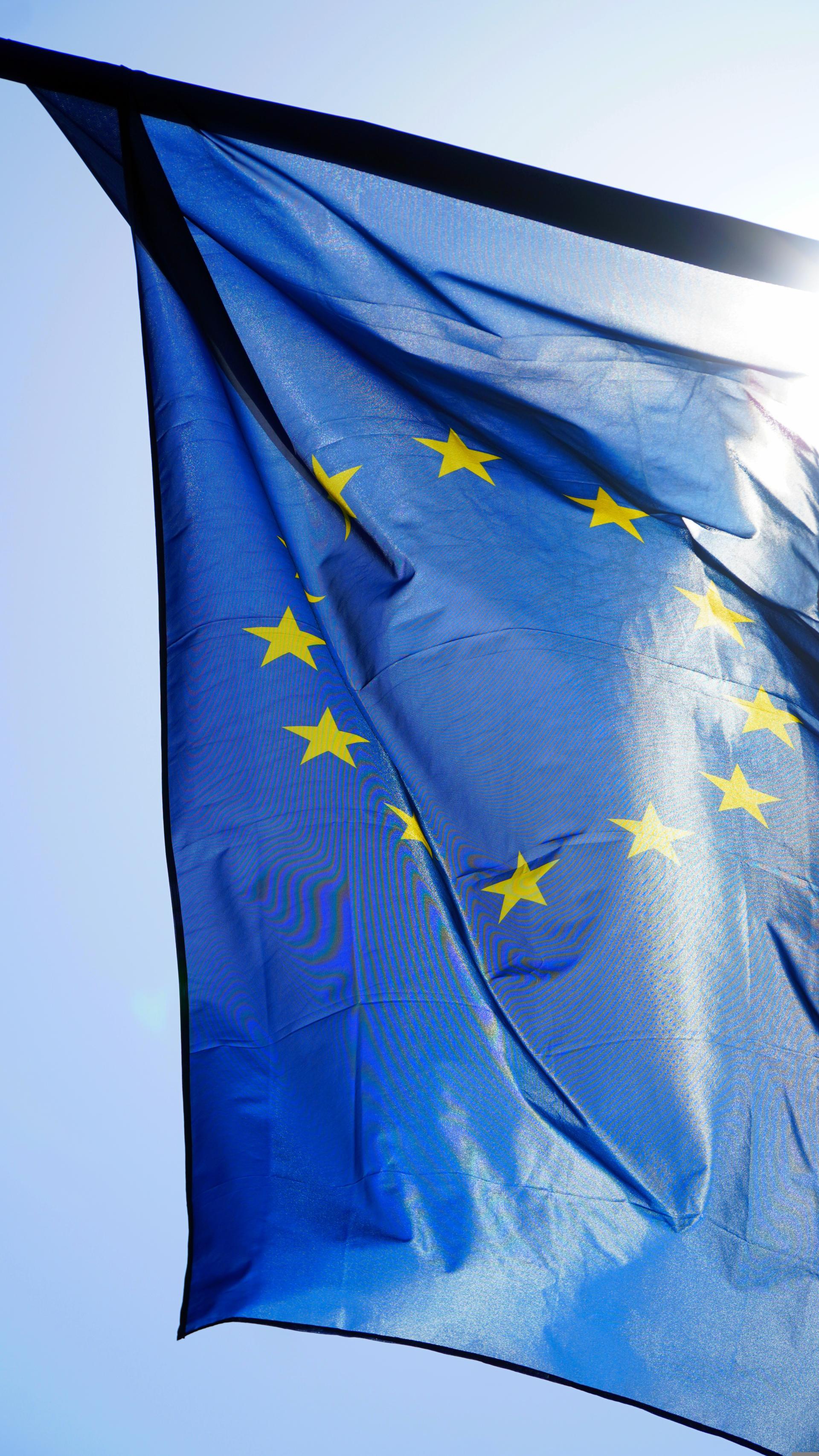 Die Europaflagge vor einem blauen, sonnigen Himmel wehend.