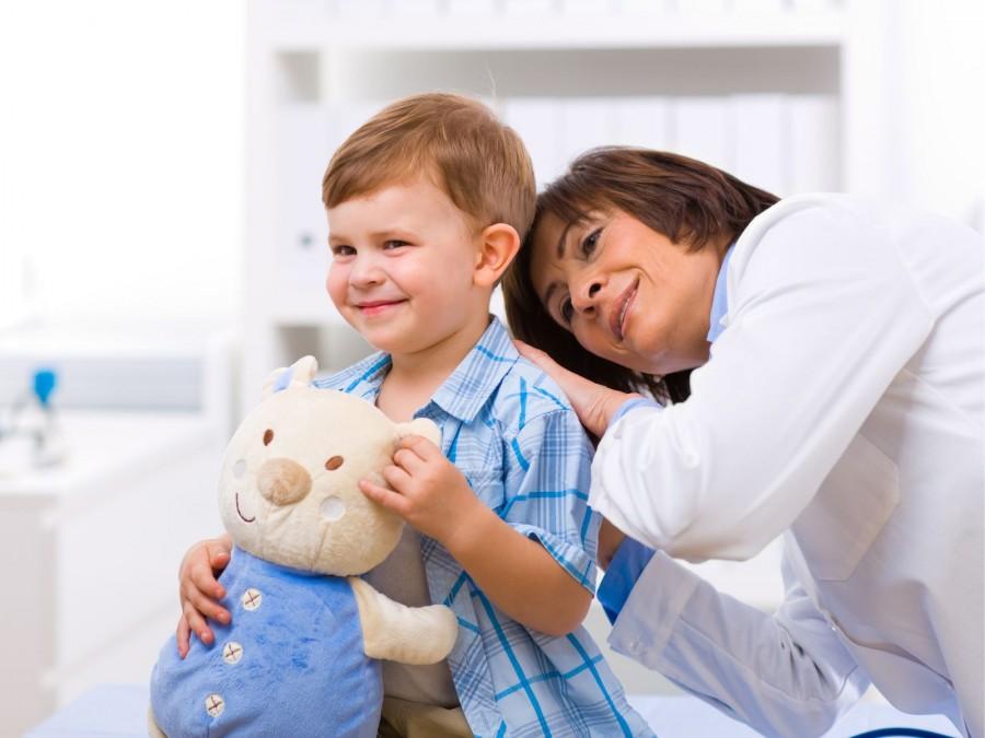 Ärztin untersucht einen kleinen Jungen mit einem Teddy auf dem Arm in der Kinderarztpraxis