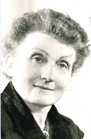 Auf dem Foto ist eine ältere Dame mit kurzen, nach hinten gelegten Haaren zu sehen.