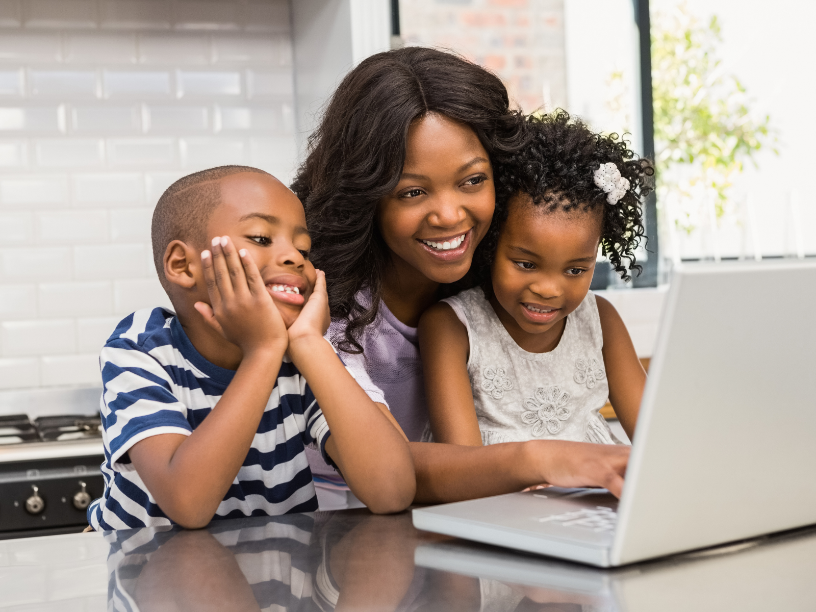 Mutter mit Kindern sitzt am Laptop und lacht.