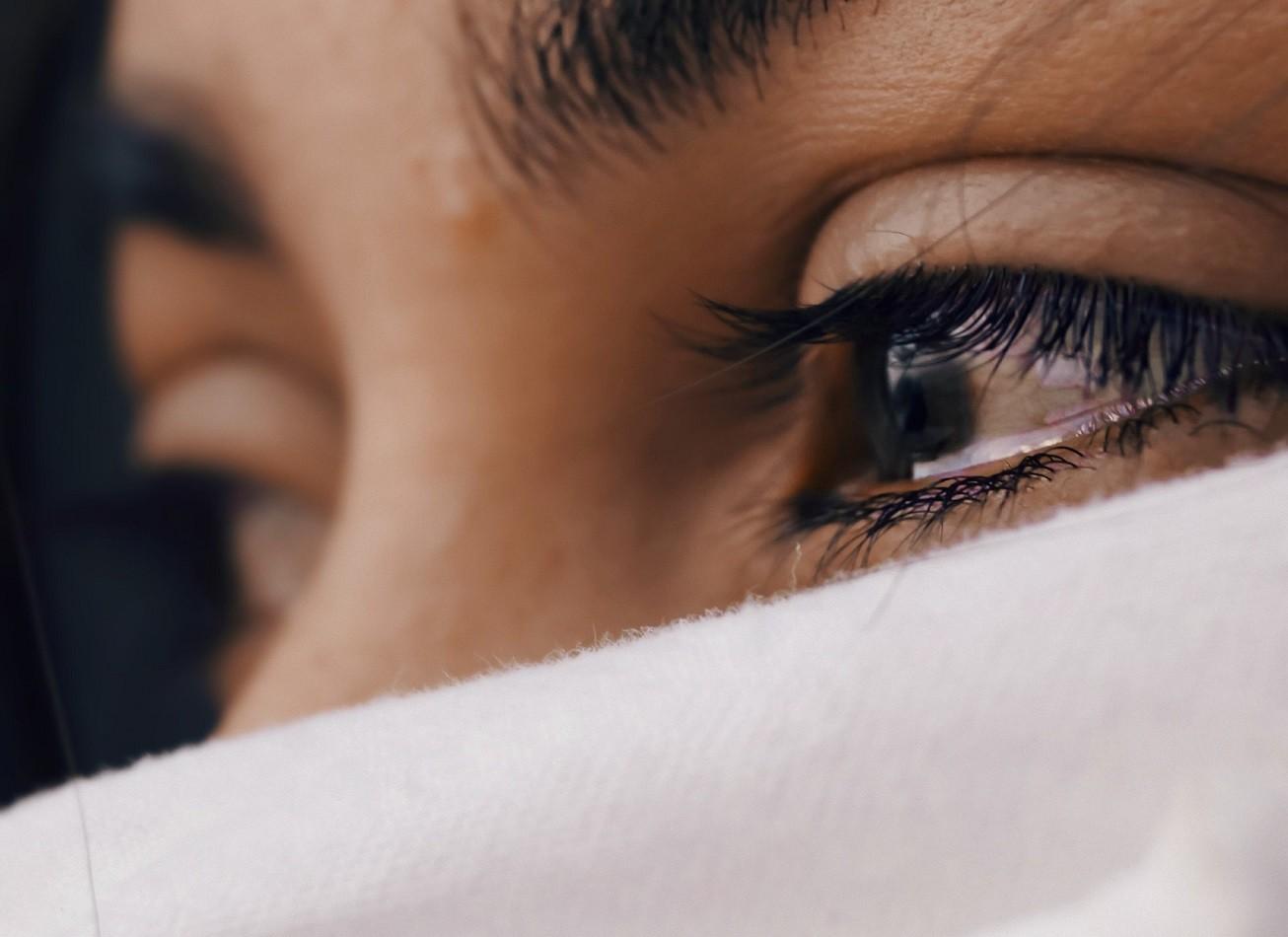 Bildausschnitt, tränengefüllte Augen einer Frau, mit weißem Tuch vor Mund und Nase.