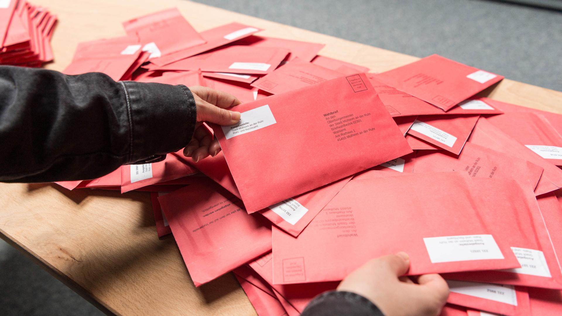 Person hält roten Wahlbrief über Tisch mit vielen weiteren roten Wahlbriefen zur Europawahl