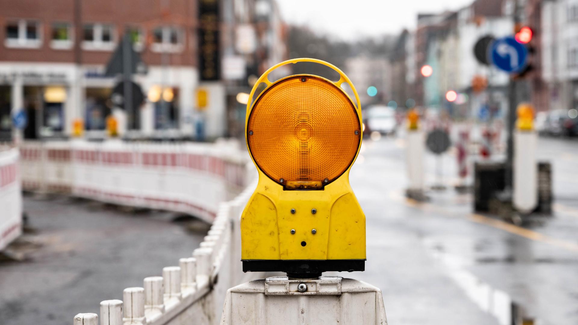 Gelbe Warnleuchte auf Baustellenabsperrung an einer nassen Straße in der Stadt