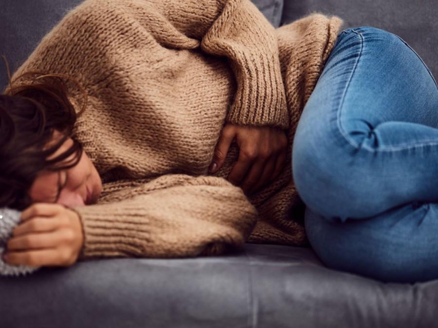 Eine Frau liegt mit Bauchkrämpfen gekrümmt vor Schmerz auf dem Sofa.