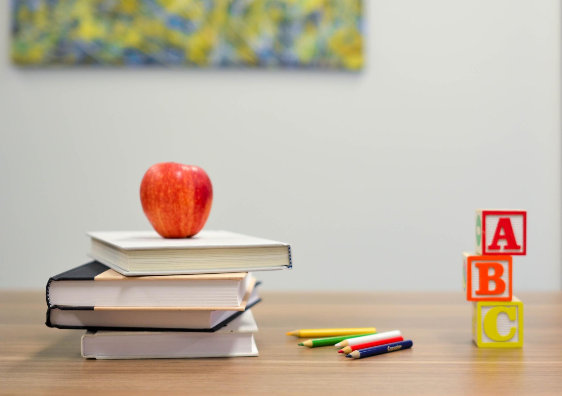 Roter Apfel auf vier Büchern, daneben liegen Stifte