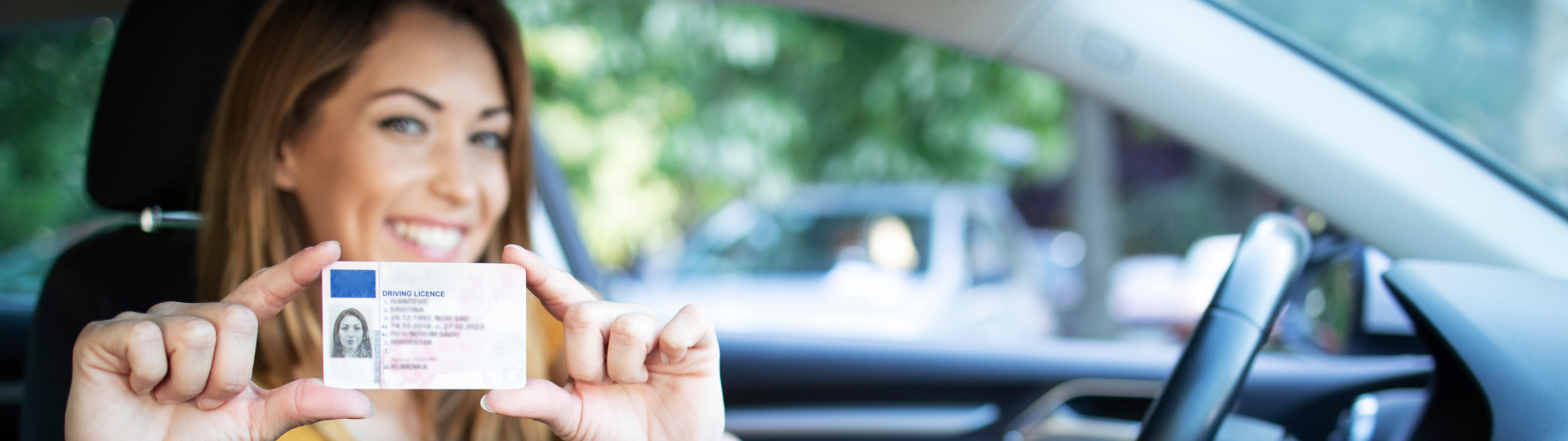 Eine Frau sitzt in einem Auto und zeigt mit einem Lächeln ihren Führerschein