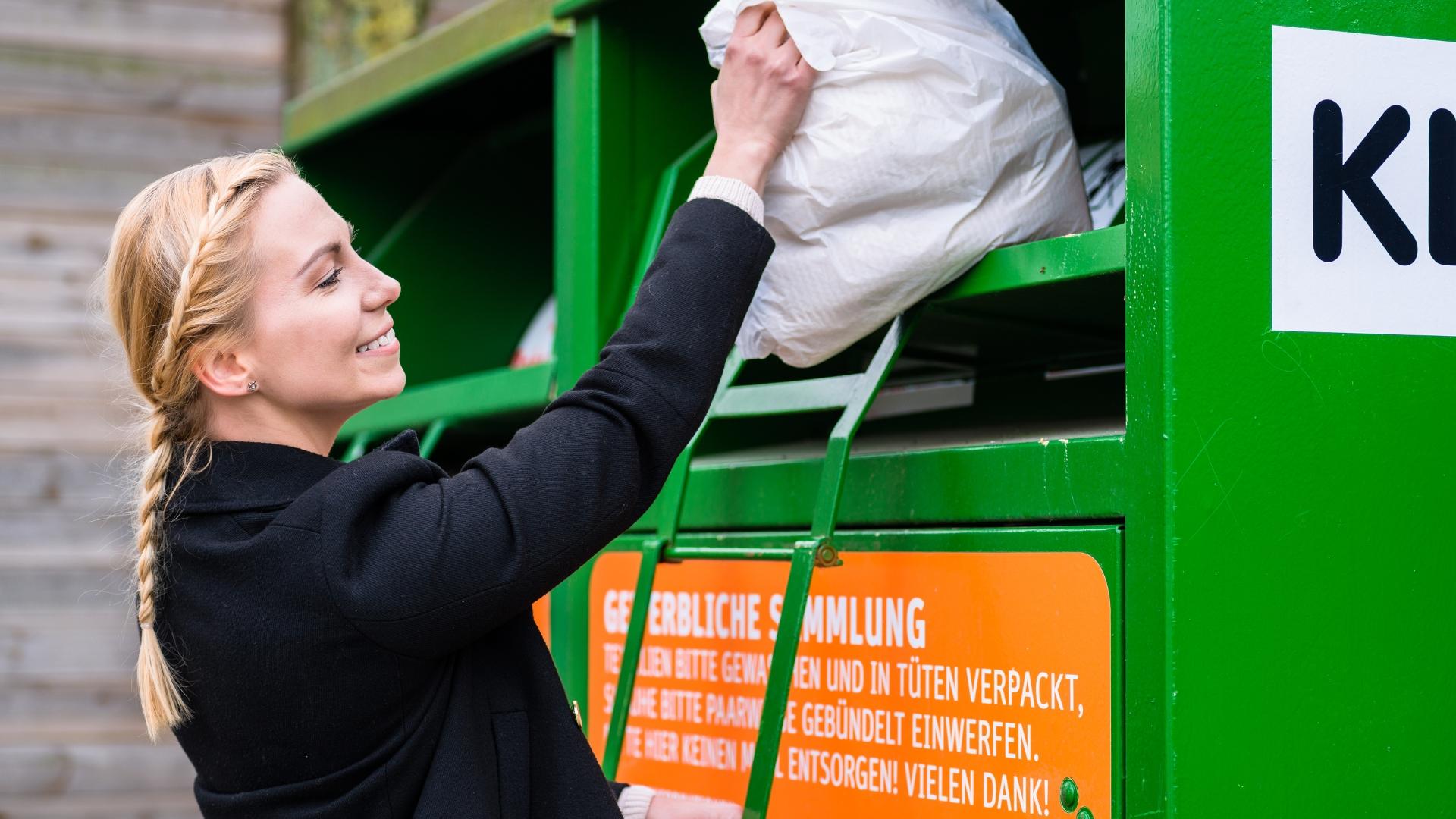 Eine Frau wirft einen Beutel in einen Altkleidercontainer.