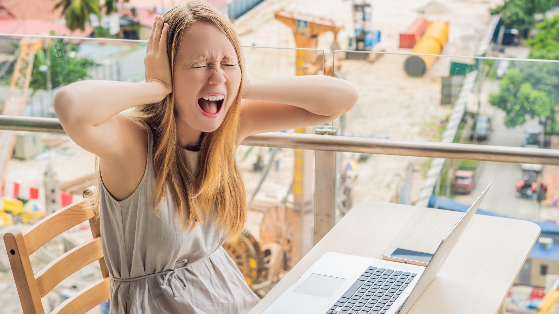 Eine Frau hält sich auf einem Balkon sitzend die Ohren zu und stößt einen Schrei aus.