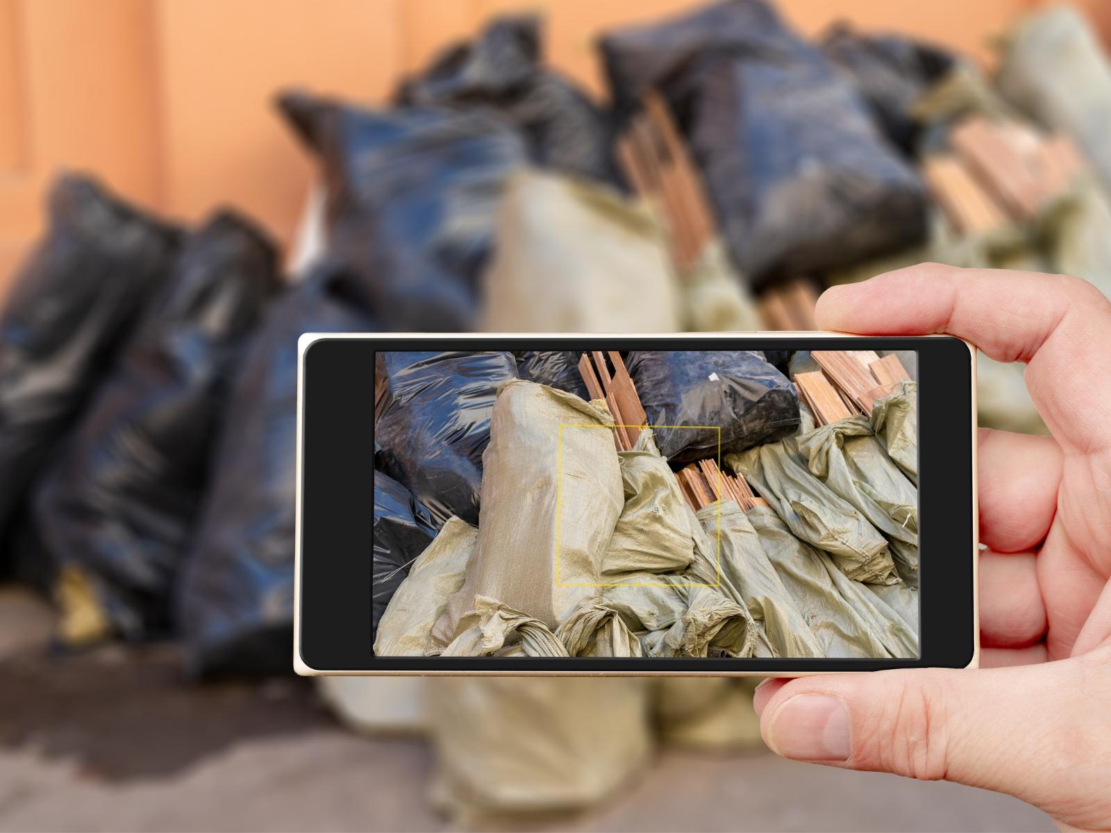 Ein in der gehaltenes Mobiltelefon fotografiert eine Müllansammlung