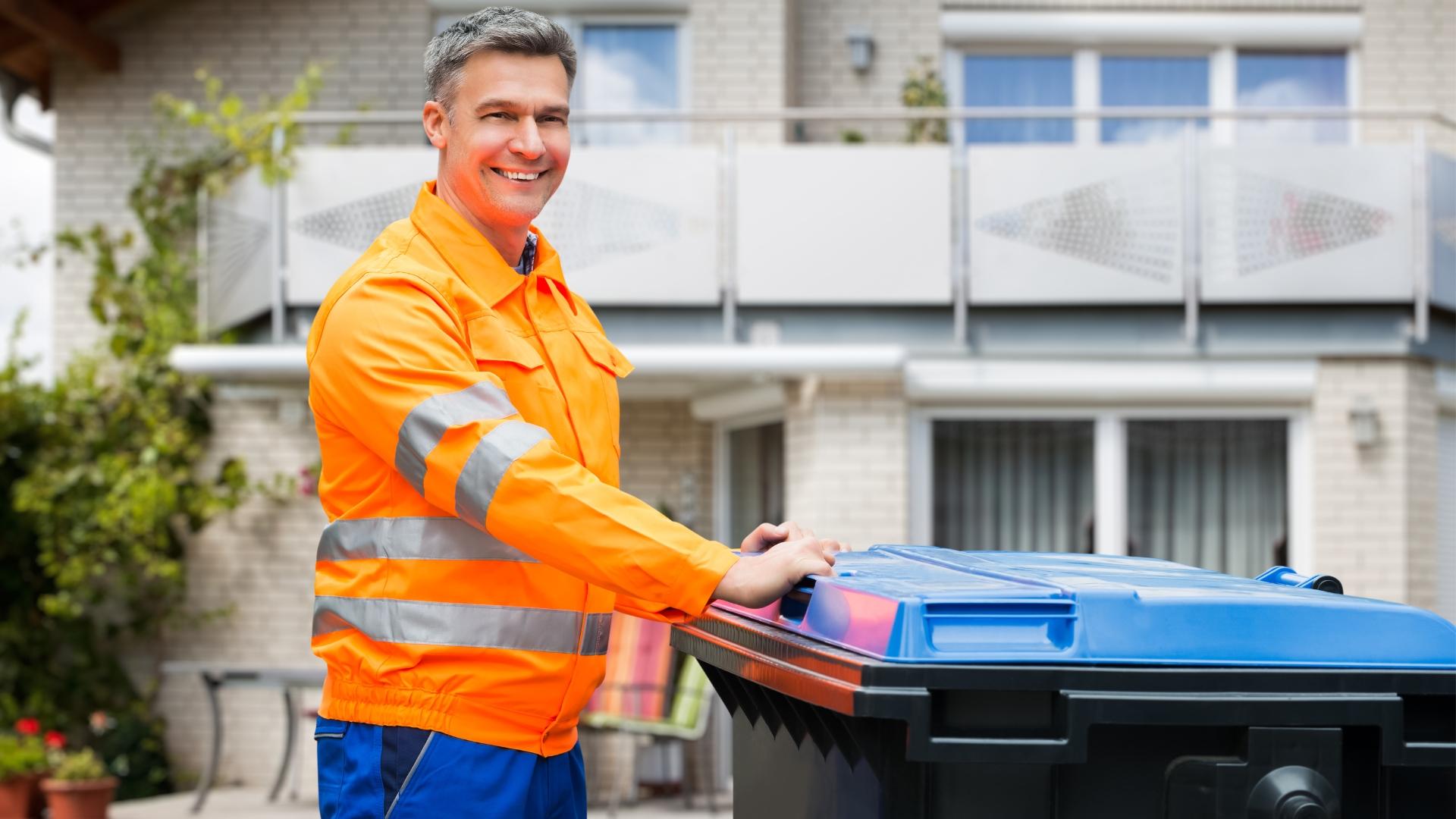 Ein Mitarbeiter der Müllabfuhr neben einer blauen Tonne.