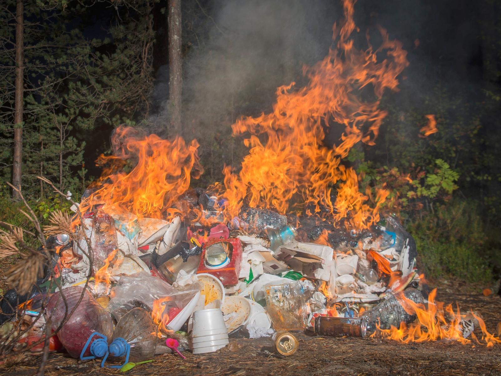 Eine Aufhäufung von Abfällen steht vor der Kulisse eines Waldes in Flammen.
