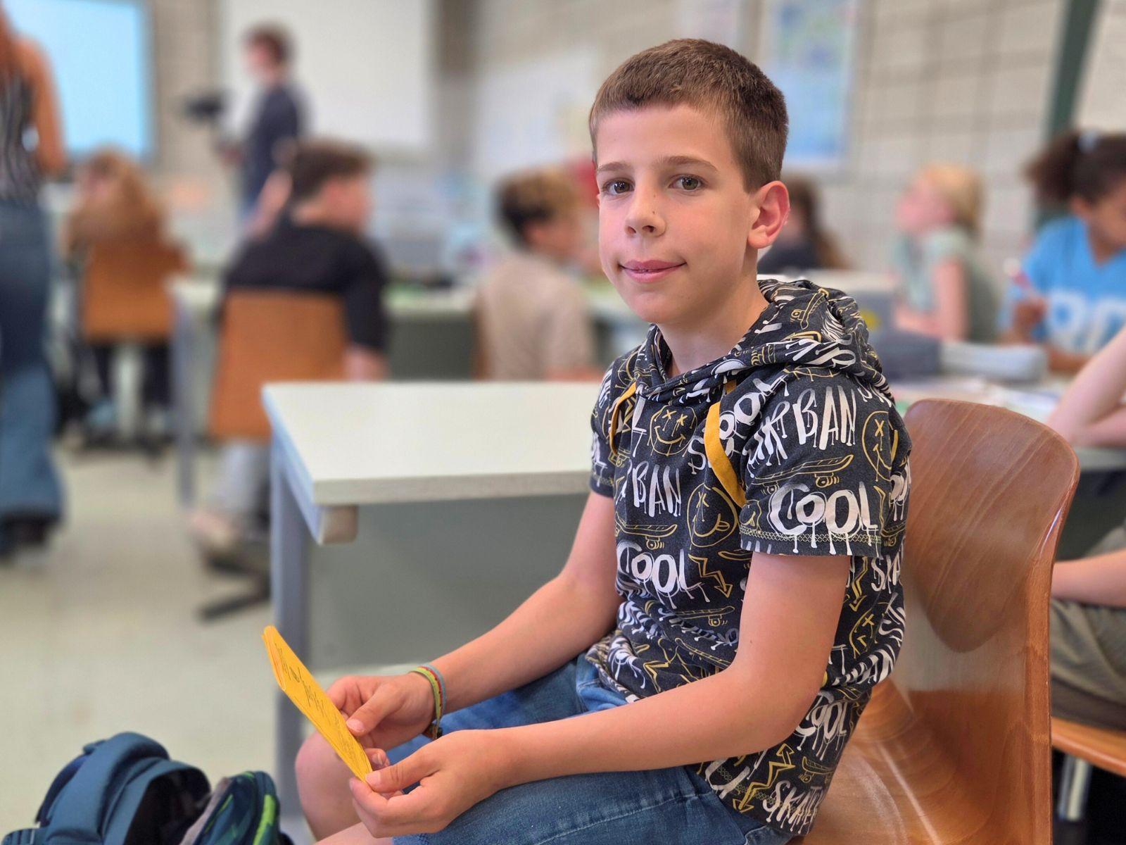 Ein Junge sitzt mit seinem Impfpass im Klassenraum und wartet auf die Kontrolle seiner Impfdaten.