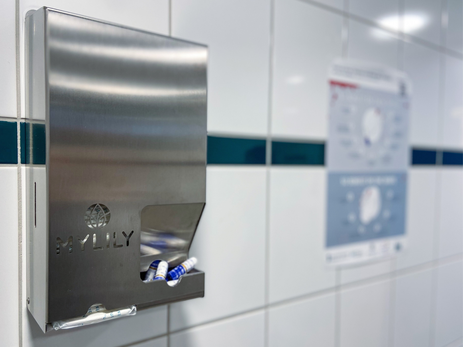 Das Foto zeigt den Spender für Tampons und Binden. Im Hintergrund ist noch das Plakat mit der Anleitung zur Benutzung von Tampons und Binden zu sehen.
