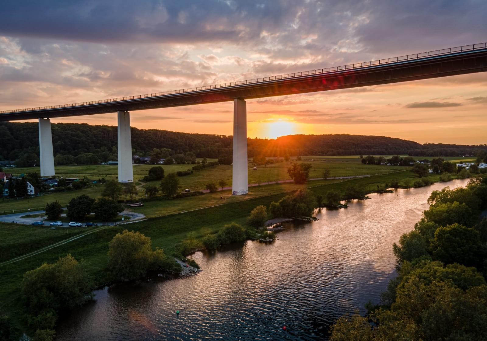 Rotgefärbter Himmel beim Sonnenuntergang an der Ruhrtalbrücke in Mülheim. Im Vordergrund der Flusslauf der Ruhr.